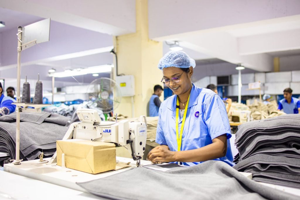 Workers in a textile factory operating sewing machines, wearing blue uniforms and caps.